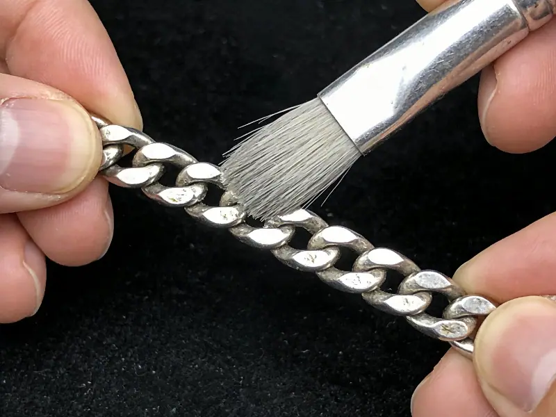 A professional demonstration of gently scrubbing a John Hardy woven silver chain using a soft brush to remove dirt and body oils.